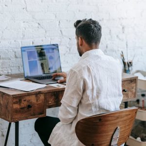 Back view unrecognizable male in formal wear working on modern netbook while sitting at desk in light room